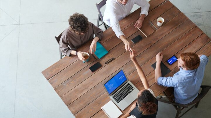 Tisch an dem Menschen mit Laptops sitzen fotografiert von oben.